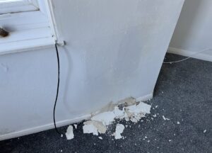 Peeling plaster on wall caused by penetrating damp in a North East England home, showing damage typical of damp issues